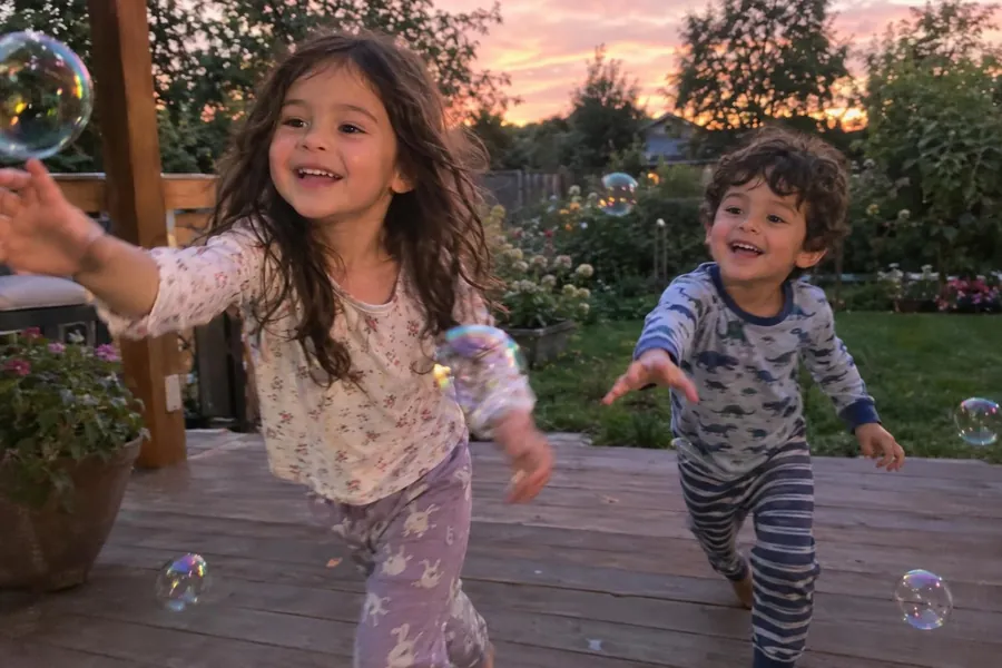 Two kids chasing bubbles on the deck at sunset, saved as a photo memory in Momora