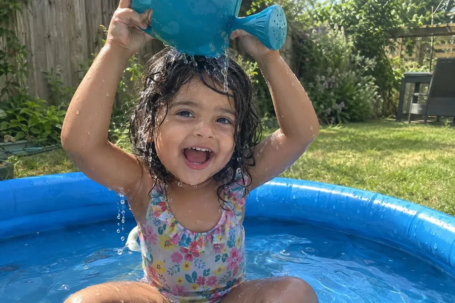Maya pouring a watering can over her head in a paddling pool